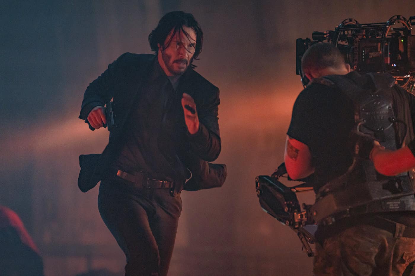 Keanu Reeves agiert gegenüber Kameraoperator James Frater am rot und blau beleuchteten Set von John Wick: Kapitel 4.