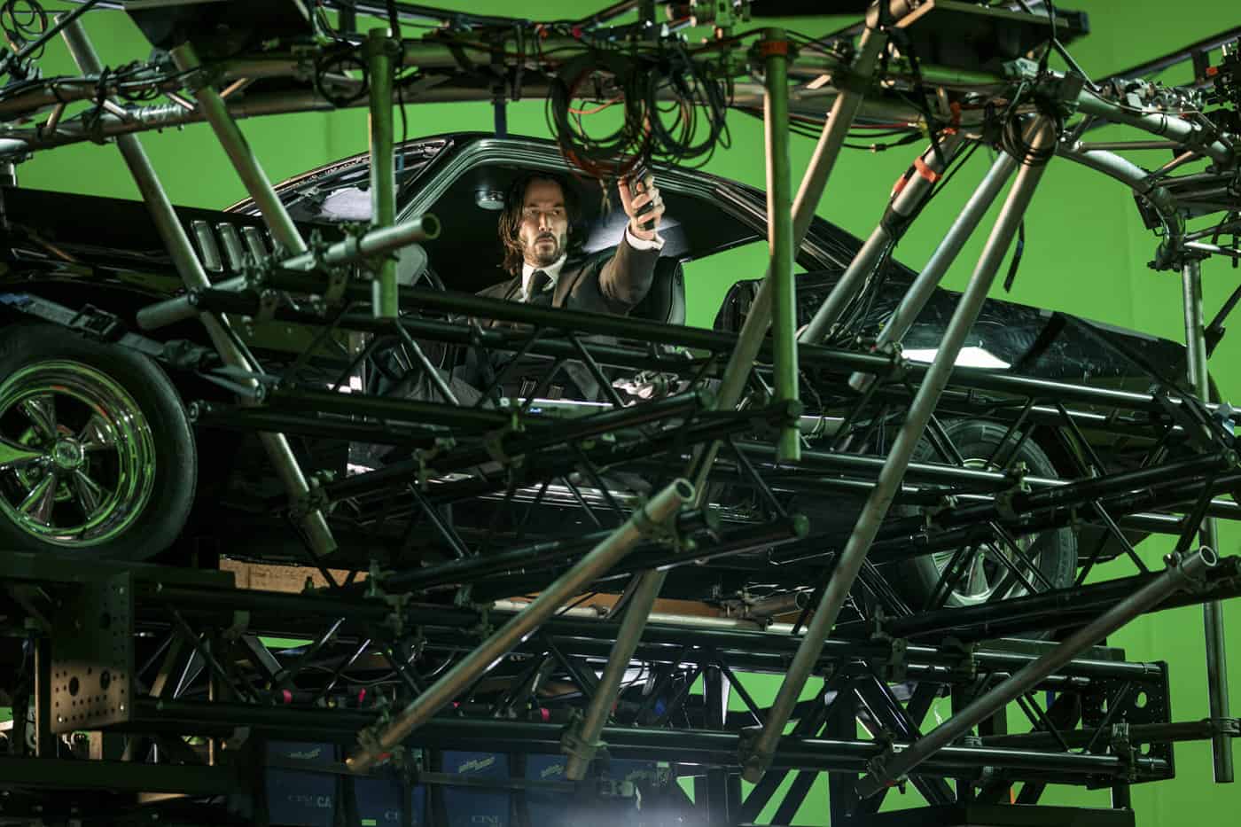Keanu Reeves sitzt bei den Dreharbeiten zu John Wick: Kapitel 4 in einem Auto zwischen Rig, Kabeln und Greenscreen.