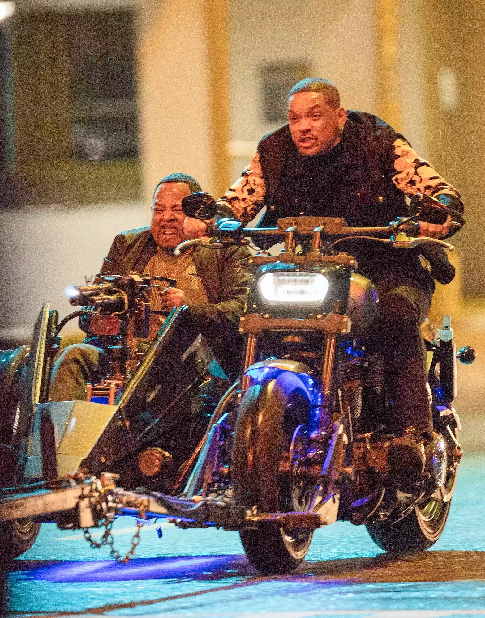 Will Smith drives a motorcycle while Martin Lawrence rides in the sidecar and aims a prop firearm on the Bad Boys for Life set.