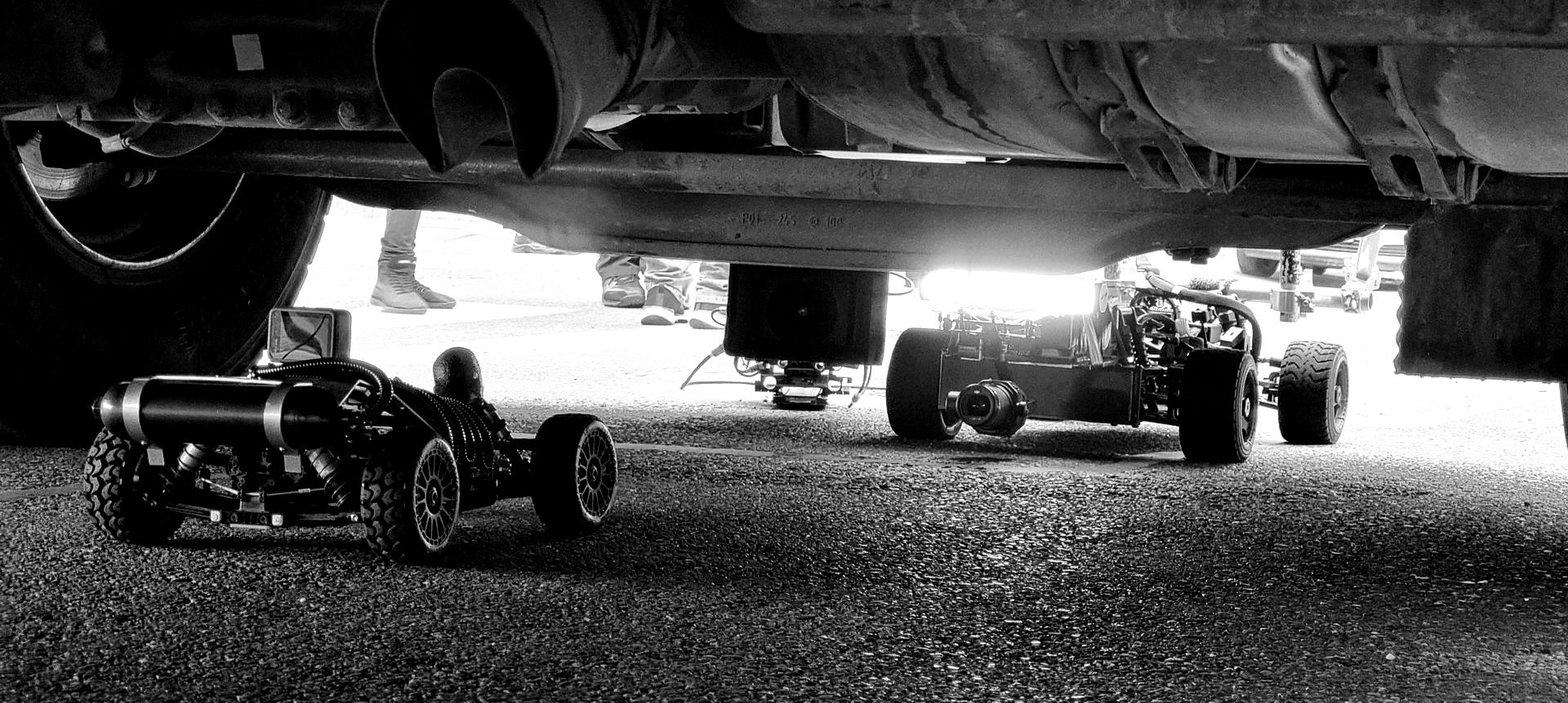 A low-slung WarpCam remote camera car drives beneath the rear of a stunt vehicle during production of Fast X.