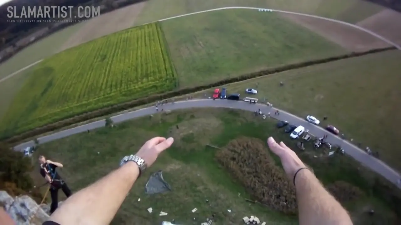 First-person view of Ferdi Fischer's hands at the Burgsteinfelsen cliff edge, looking down toward the cardboard landing stack 45 metres below.