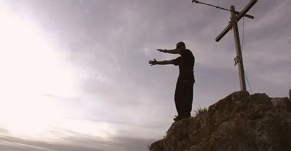 Ferdi Fischer stands below the summit cross at the cliff edge seconds before the jump.