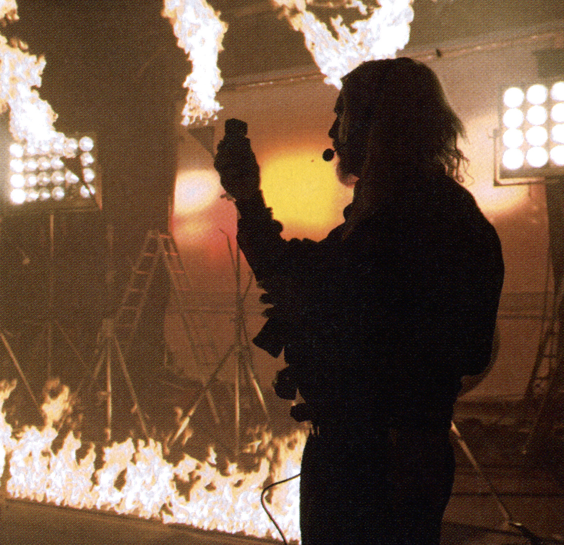 Robert Richardson holds a light meter on the Inglourious Basterds cinema set, with flames and production lights behind him.