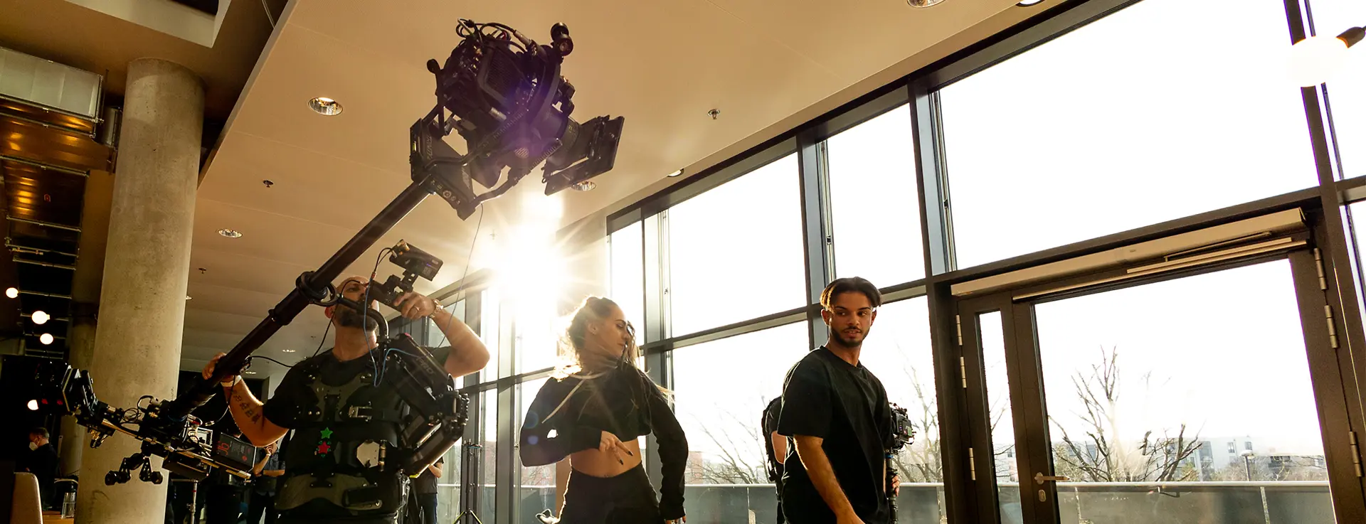 An operator uses an ARRI TRINITY 2 body-worn stabilizer while filming dancers inside a bright hall.