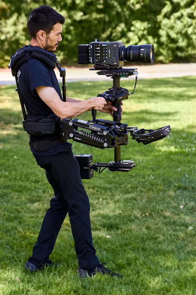 A camera operator walks outdoors with a body-worn Steadicam fitted with the Volt 3 stabilization system.