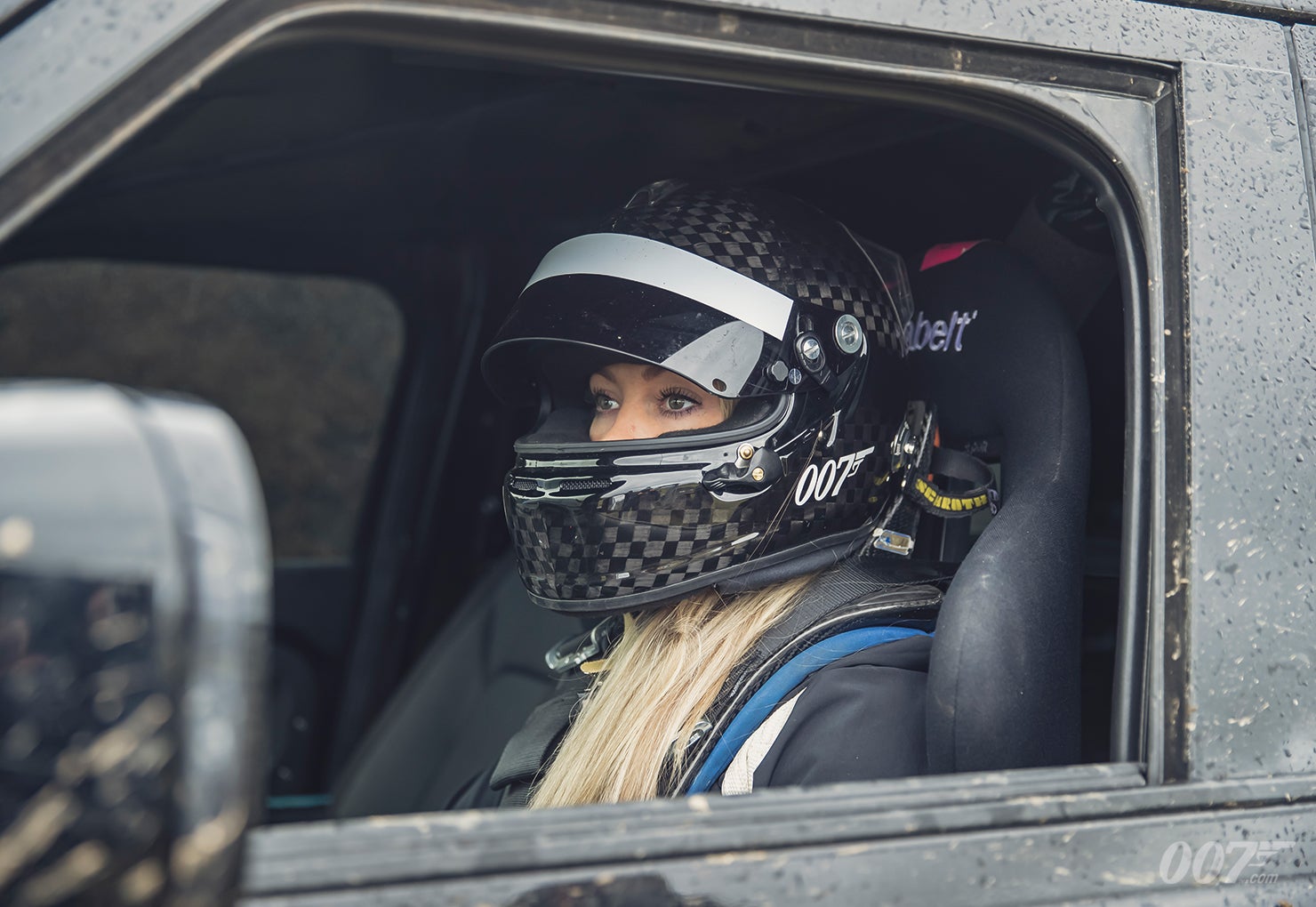 Stunt driver Jessica Hawkins sits helmeted and harnessed inside a Land Rover Defender during No Time To Die testing.