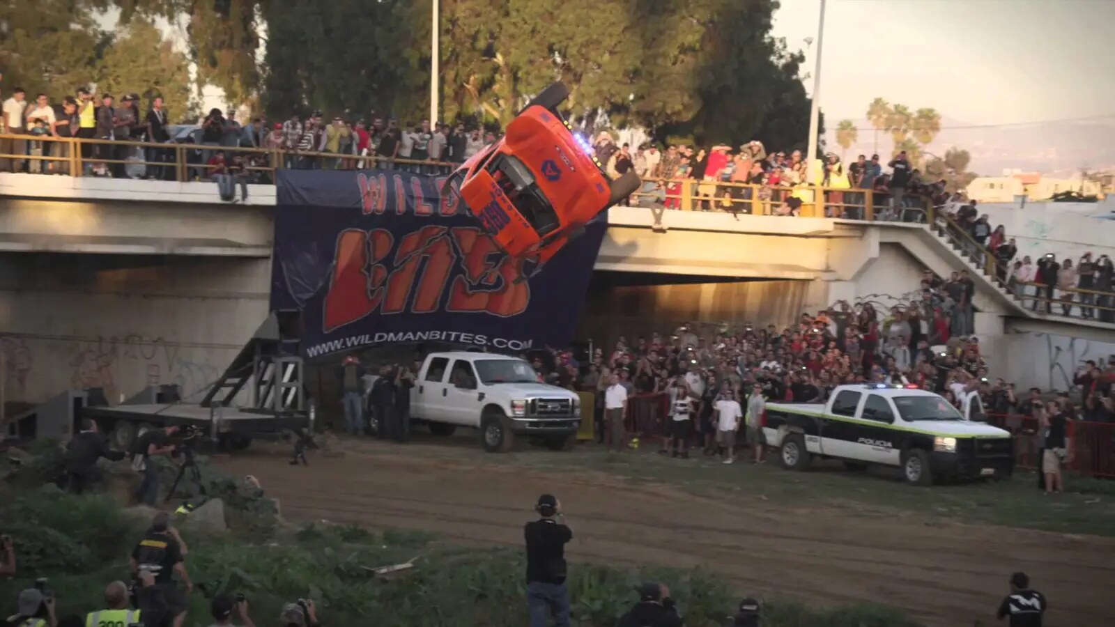 A red pickup truck rotates through a mid-air barrel roll above an arena while the landing area and spectators remain visible.
