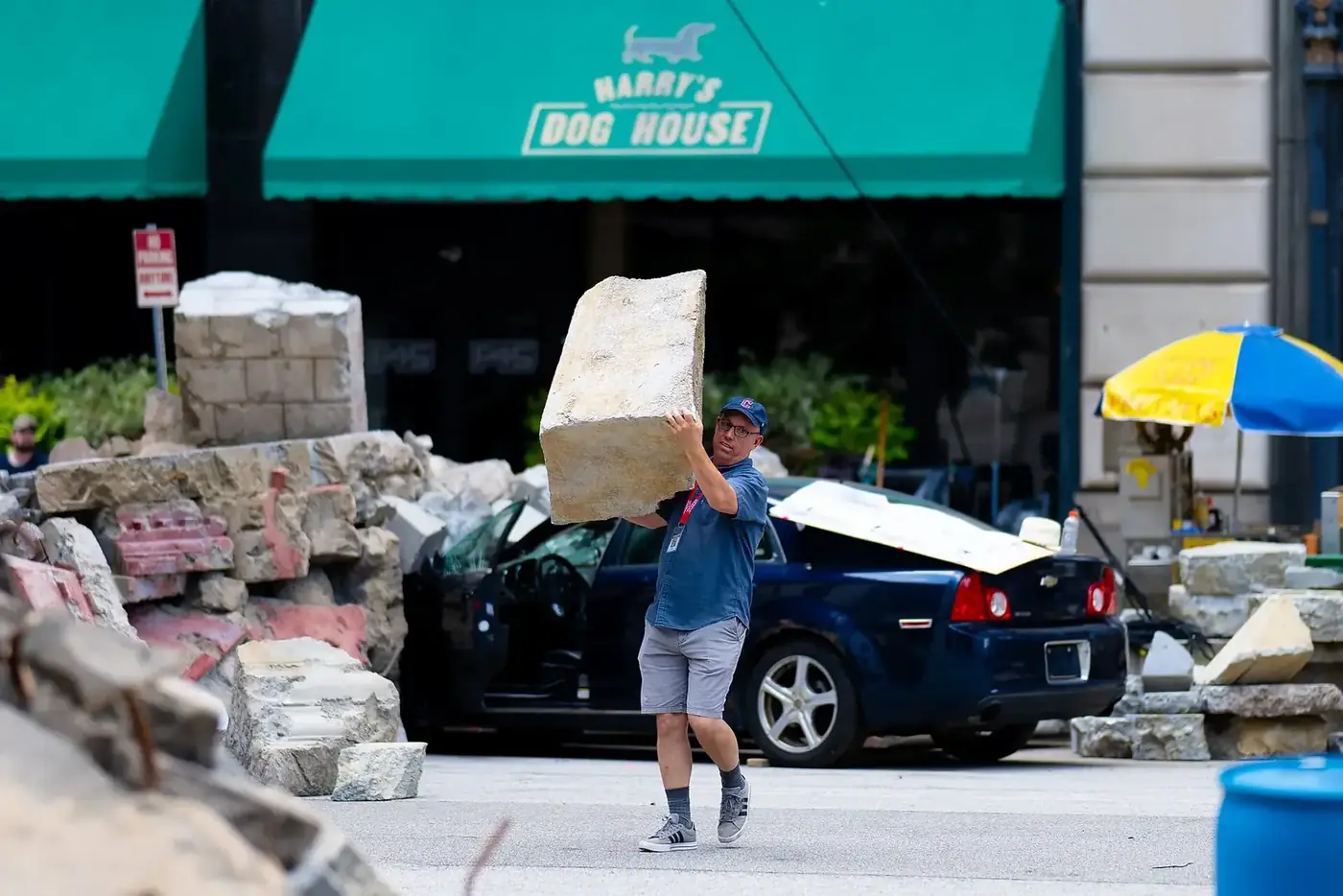 A crew member carries concrete-look prop debris past rubble and a wrecked car on the Cleveland set of Superman.