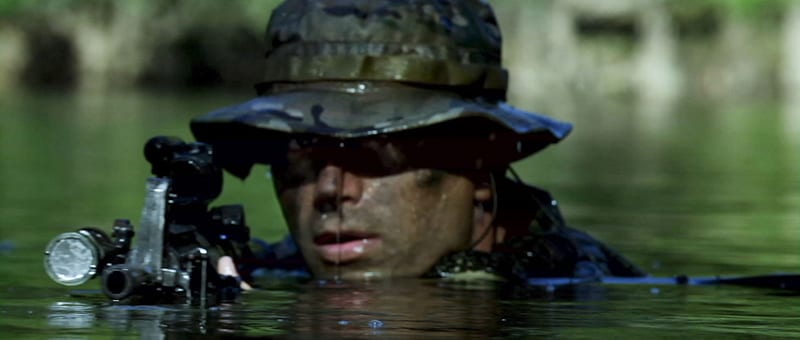 A Navy SEAL moves almost fully submerged through green water, with his face and rifle held just above the surface, in Act of Valor.