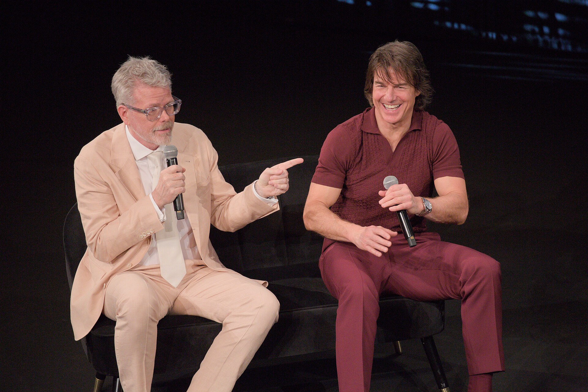 Christopher McQuarrie zeigt auf Tom Cruise, während beide bei einem Cannes-Gespräch 2025 zu Mission: Impossible — The Final Reckoning Mikrofone halten.